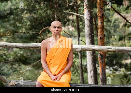 buddista seduto su una panca di tronchi e meditando con occhi chiusi nella foresta Foto Stock