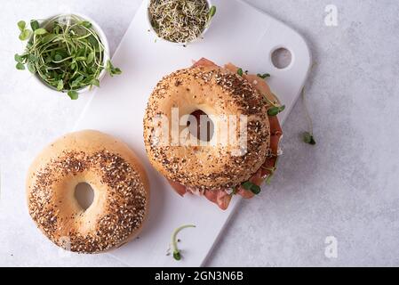 Due bagel e una ciotola con microgreens su un tagliere, panini su sfondo bianco, vista dall'alto. Foto Stock