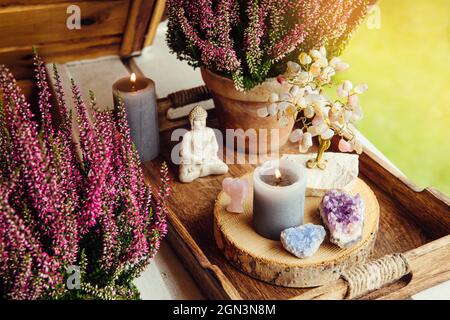 Decorazione spirituale casa balcone con fiori rosa di erica, fiamma a lume di candela, geodi di cristallo, albero di cristallo e piccola statuetta Buddha. Cute autunno sp Foto Stock