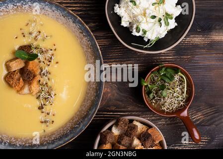 Deliziosa zuppa di crema di zucca decorata con crostini, formaggio e microgreens su sfondo di legno scuro, zuppa di purea vegetariana, cibo sano. Foto Stock