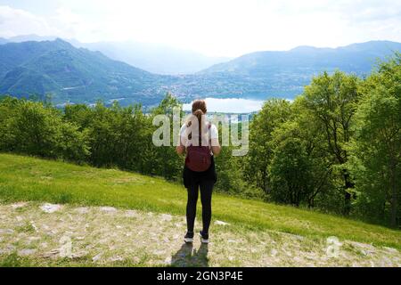 Donna escursionista in piedi sul sentiero e guarda con soddisfazione dalla cima della montagna il lago Foto Stock