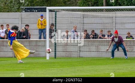 L'uomo vestito come bianco neve prende una penalità con un nano in gol ad una festa di Pag al Trafford FC Foto Stock