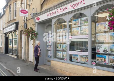 Viste di Winchcomber una piccola città di mercato del Cotswold in Gloucestershire, Regno Unito donna matura che guarda nella finestra dell'agente immobiliare Foto Stock