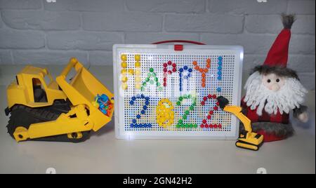 happy 2022 foderato con mosaico di plastica colorata. Babbo natale, apripista giallo giocattolo e escavatore . Realizzato da mani di bambini, idee per la creatività con ch Foto Stock