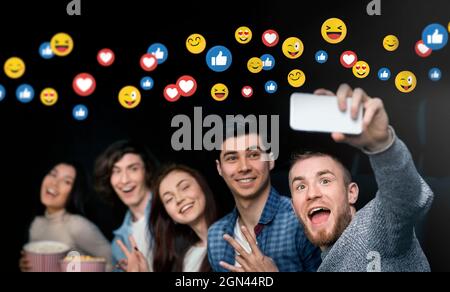 Felice emozionale giovane gruppo di persone diverse al cinema con popcorn, divertirsi, prendere selfie Foto Stock