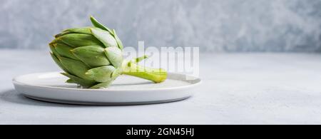 Carciofi crudi interi organici verdi bagnati su fondo grigio. Vista dall'alto con spazio. Foto Stock