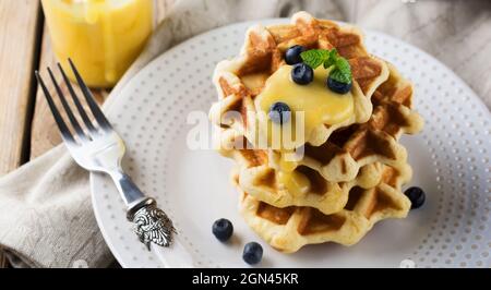 Waffle belgi al limone Kurd e mirtilli. Stile rustico. Messa a fuoco selettiva. Foto Stock