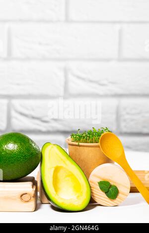 Vita morta creativa con avocado, micro verde e cucchiaio su sfondo bianco con supporti e podi in legno. Equilibrio cibo sano. Bilanciato Foto Stock