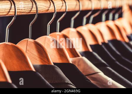 Abiti da uomo in diversi colori appesi su un appendiabiti in un negozio di abbigliamento al dettaglio, primo piano. Camicie da uomo, vestito appeso al rack. Foto Stock