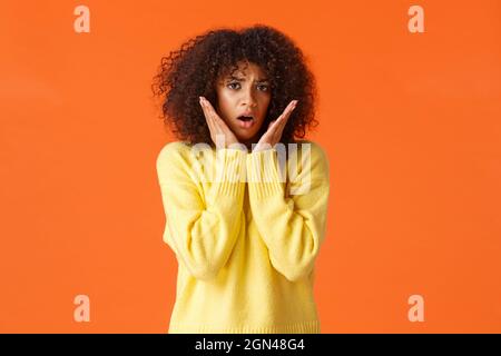 Spaventata timida e insicura bella ragazza giovane con taglio di capelli afro, maglione giallo, affannosa scioccato e interessati, toccando e fissando in preda al panico fotocamera Foto Stock