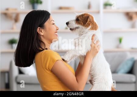 Emotiva donna asiatica accarezzando il suo cane carino a casa, primo piano Foto Stock