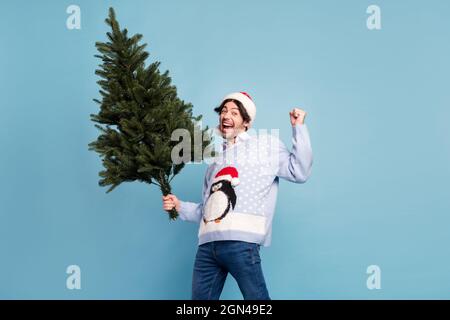 Foto di positivo allegro uomo felice vincitore tenere mano natale albero verde isolato su sfondo blu Foto Stock