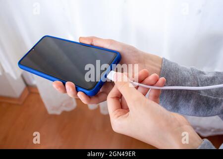 La giovane donna collega il telefono al caricabatterie. Foto Stock