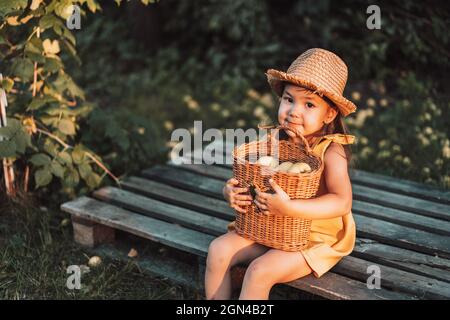 Bambina in cappello di paglia abbraccia un cestino di vimini con pere Foto Stock