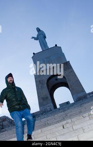 il giovane uomo scende per qualche scalinata su una collina in una città dove in cima c'è una statua Foto Stock
