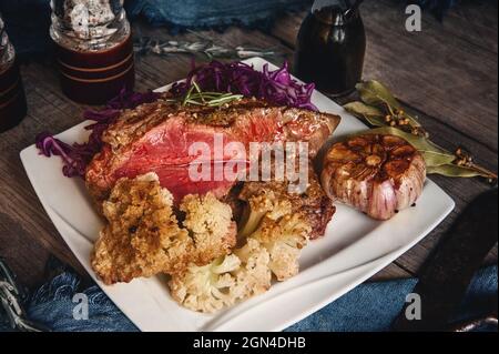 Bistecca di carne arrosto leggera con verdure. La carne succosa è su un piatto con un contorno di cavolfiore, cavolo rosso e aglio al forno. Foto Stock