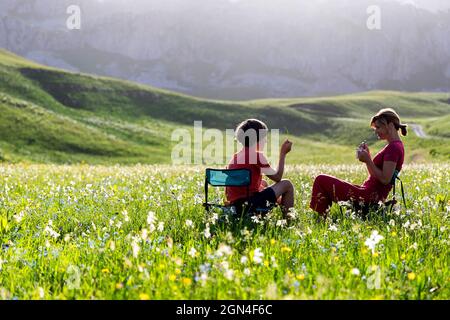 Due turisti seduti su sedie e che si godono la colazione in un prato stupendo pieno di giunchiglie selvatiche vicino al lago Kapetanovo. Foto Stock