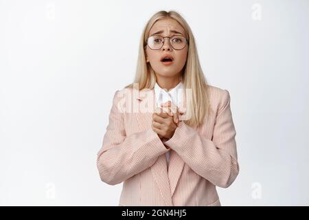 Lavoratore impressionabile dell'ufficio femminile in vetri e vestito, piangendo e implorando qualcosa, dica prego, levandosi in piedi sopra sfondo bianco Foto Stock