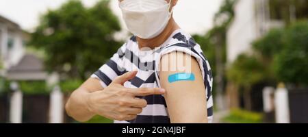 Giovane uomo asiatico che indossa la maschera di protezione del viso COVID-19 che punta al bendaggio dopo aver ricevuto il vaccino durante il giorno - dimensione banner panoramico Foto Stock