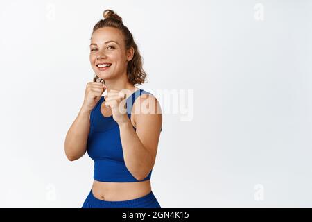 Felice atleta femminile in piedi in posa da caccia, ombra boxing e ridere, facendo esercizi di fitness in abbigliamento sportivo, in piedi su sfondo bianco Foto Stock