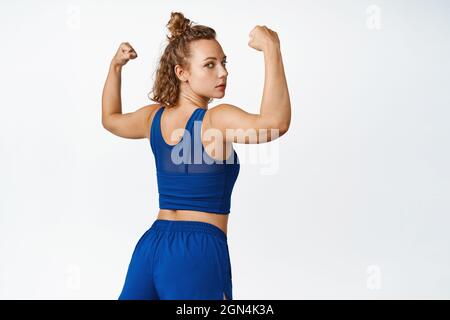 Il bicipite flessibile dallo sportivo è sicuro e mostra braccia forti. Vista posteriore dei muscoli show-off della donna di idoneità, si leva in activewear su sfondo bianco Foto Stock