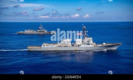 I marinai della Marina degli Stati Uniti a bordo del cacciatorpediniere missilistico guidato di classe Arleigh Burke USS Chafee, di fronte, impazzano le rotaie in preparazione di una cerimonia d'onore con il cacciatorpediniere JS Ikazuchi della Japan Maritime Self-Defence Force, di classe Murasame, durante le operazioni congiunte il 19 settembre 2021 nel Mare delle Filippine. Foto Stock