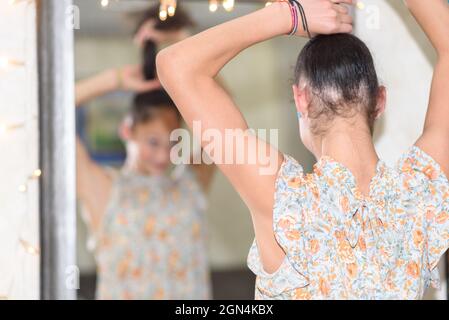 Vista posteriore di una ragazza adolescente con riflesso sfocato nello specchio che fa un ponytail. Foto Stock