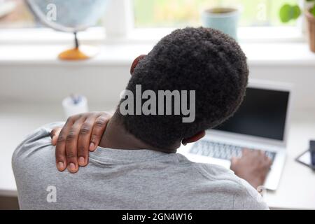 Vista posteriore dell'uomo a casa che lavora sul collo del fregio del laptop e sul Tiro nel dolore Foto Stock