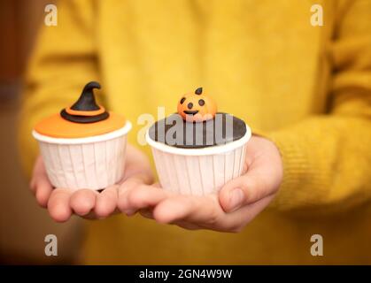 Un bambino sta tenendo i muffin di Halloween con le decorazioni nella forma di una zucca e di un cappello della strega. Set di cupcakes per le vacanze e dolcetti di Halloween. Foto Stock