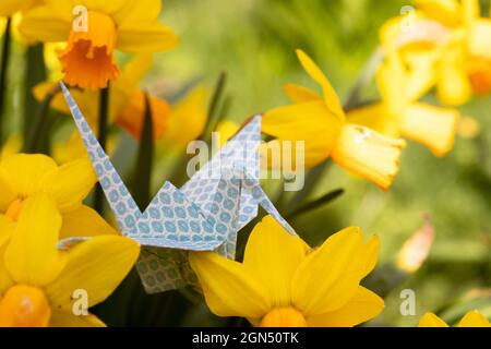 Primo piano di una gru di carta origami seduta sull'erba tra fioritura dei primi fioritori che simboleggiano l'ora di primavera, un nuovo inizio e speranza Foto Stock