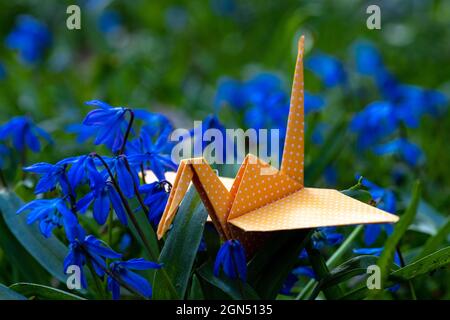 Primo piano di una gru di carta origami seduta sull'erba tra fioritura dei primi fioritori che simboleggiano l'ora di primavera, un nuovo inizio e speranza Foto Stock