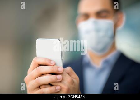 Smartphone moderno in mani inriconoscibili uomo d'affari, uomo che indossa maschera facciale Foto Stock