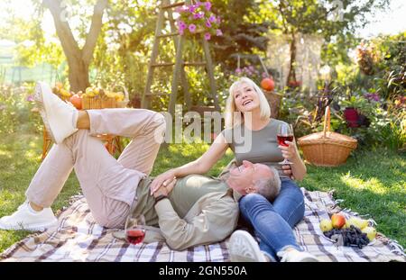 Romantico sposi anziani godersi un picnic insieme, riposare su coperta in giardino e bere vino rosso, spazio libero Foto Stock