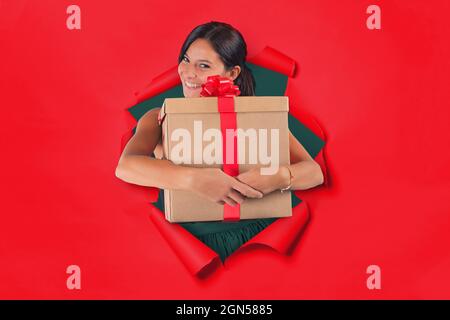 Donna all'interno di un buco su uno sfondo di carta rossa tiene stretto nelle sue braccia un pacchetto regalo Foto Stock