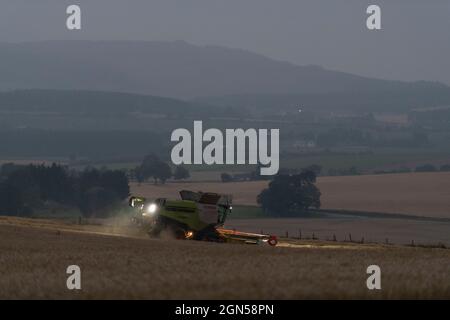 Una vista attraverso la campagna dell'Aberdeenshire con una mietitrebbia che opera in un campo di Barley a Dusk Foto Stock