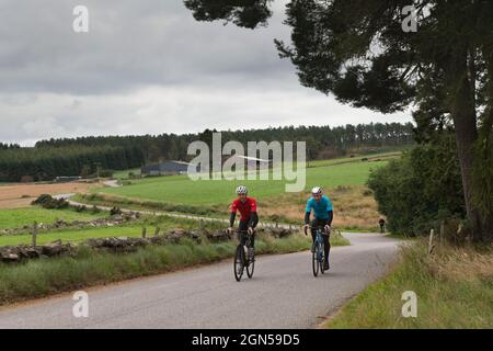 Due ciclisti maschili da rictreational in bicicletta lungo una Country Lane che si snoda attraverso i terreni agricoli nella campagna dell'Aberdeenshire Foto Stock