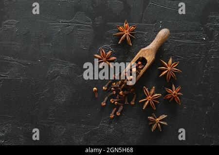 Cannella, chiodi di garofano e anice stellato. Spezie diverse su sfondo nero. Messa a fuoco selettiva. Con paletta in legno. Foto Stock