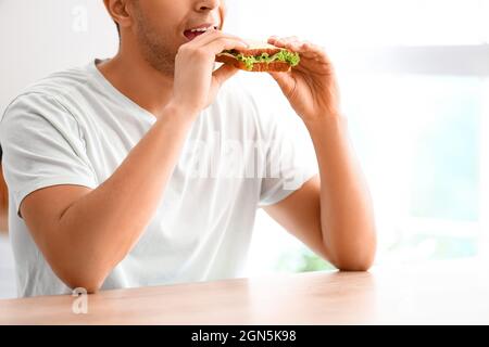 Giovane uomo che mangia gustoso sandwich in cucina Foto Stock