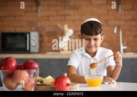 Ragazzino che mangia mele, miele e melograni a casa. Rosh Hashanah (Capodanno ebraico) celebrazione Foto Stock
