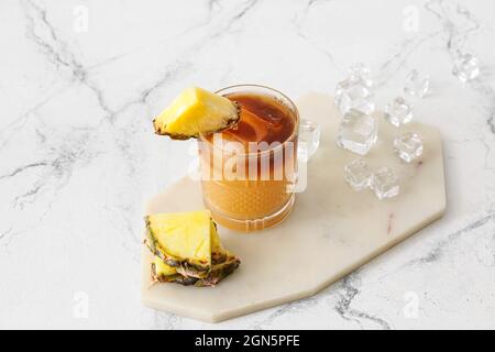 Salite a bordo con un bicchiere di delizioso cocktail mai tai, cubetti di ghiaccio sparsi e fette di ananas su un tavolo leggero Foto Stock