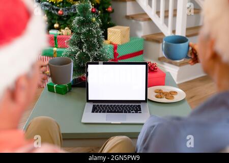 Vista posteriore della coppia anziana caucasica che usa un computer portatile, con videochiamata a natale Foto Stock