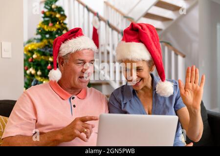 Felice coppia caucasica senior indossando santa Hat, utilizzando un computer portatile, facendo videochiamata a natale Foto Stock