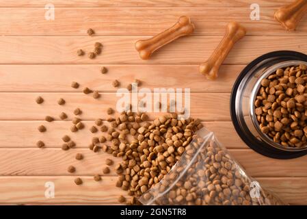 Crocchette di cani in sacchi e alimentatore su tavola di legno con ossa della pelle pressate. Vista dall'alto. Composizione orizzontale. Foto Stock