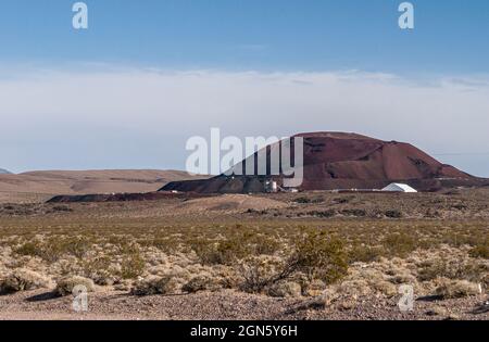 High Desert, Nevada, USA - 17 maggio 2011: Edifici di miniera bianca contro la collina di rifiuti rosso-marrone scuro sotto il paesaggio blu nuvoloso in un paesaggio secco con un po' di verde Foto Stock