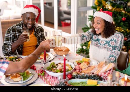 Felice coppia afroamericana che indossa cappelli di santa, facendo toast al tavolo di natale Foto Stock