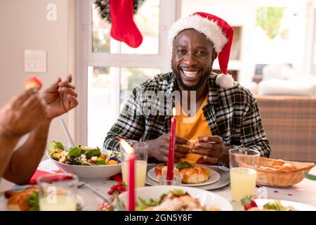 Felice uomo afroamericano che indossa il cappello di santa seduta al tavolo di natale Foto Stock