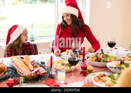 Happymother e figlia che indossano cappelli di santa seduta al tavolo di natale Foto Stock