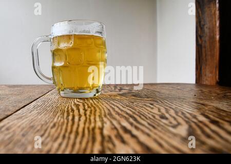 Tazza di birra con birra alla spina su un tavolo da pranzo rustico; dissetante alcolico in una giornata calda. Foto Stock