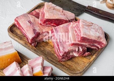 Set di costolette di manzo crudo, con ingredienti, e vecchio coltello taglierino per macellaio, su sfondo di pietra bianca Foto Stock