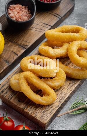 Croccante di calamari fritti o anelli di cipolle in pastella, su tavola da servire, su sfondo di tavola di pietra grigia Foto Stock